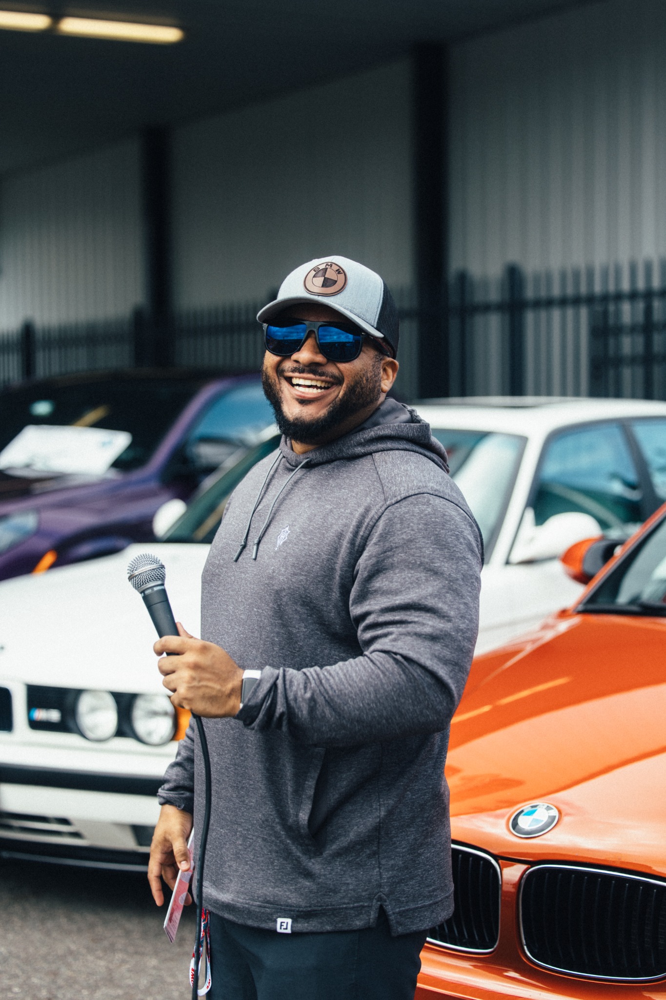 Smiling MPACT host holding a microphone in front of an orange BMW.